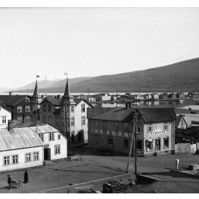 6. Kaupvangstorg eða Kaupfélagshornið um 1925. Húsið til vinstri er svokallað Dúahús en það var fyrsta íbúðarhúsið sem reis í miðbænum árið 1894. Það var rifið þegar stórhýsi KEA reis 1930. Grófargilslækurinn rann niður sunnan við húsið og á honum var brú. Við brúna stendur “Gullkistan”  og á henni stóð “Gefið svo mun yður gefast” . Gullkistan var söfnunarbaukur og í hana áttu vegfarendur að gefa fáeina aura til styrkjar ekkjum og munaðarlausum börnum. Ljósmynd Jón & Vigfús.