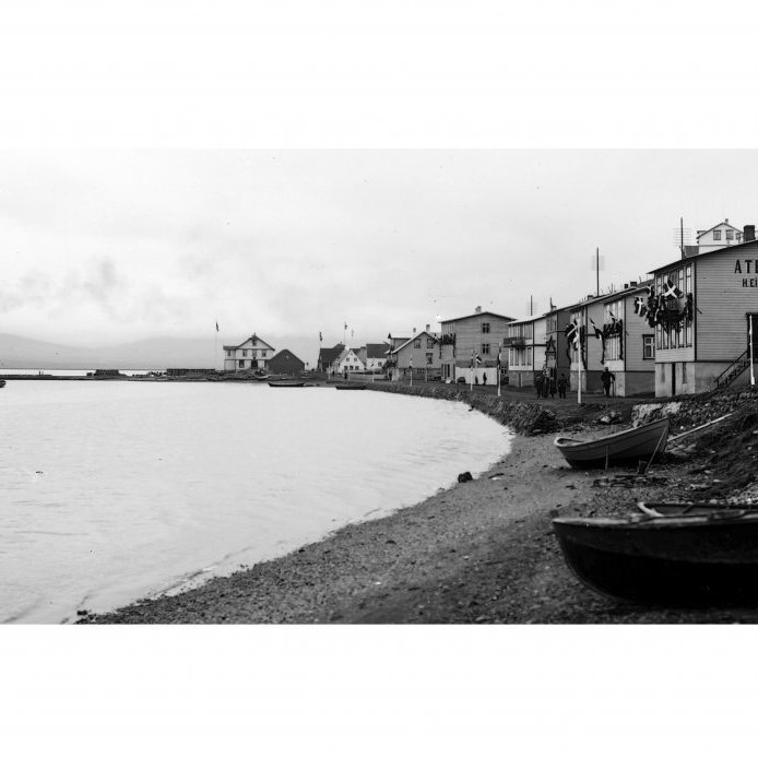 55. Húsaröðin við Hafnarstræti 19-41 í sveigðri línu meðfram fjörunni og stórhýsin á Barðsnefi. Húsin eru mikið skreytt í tilefni af komu Friðriks VIII. konungs árið 1907. Um tíma virtist sem á Barðsnefi yrði ný þungamiðja bæjarins. Þar risu stærstu húsin, Barnaskólinn árið 1900 og Samkomuhúsið árið 1906. Norðan við Samkomuhúsið í brekkunni stóðu svo Bogahúsið (reist 1898 og 1902) og Hafnarstræti 66 (1897). Bogahúsið var rifið árið 1980 en Hafnarstræti 66 brann árið 1952. Á Torfunefsbryggu má sjá glytta í hliðið sem reist var vegna landgöngu konungs. Ljósmynd Hallgímur Einarsson.