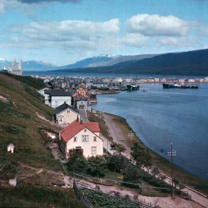 56. Fyrsta litmyndin af Akureyri árið 1943. Þarna sést í gaflinn á Sýslumannshúsinu og Barnaskólanum sem að þá hýsti Amtsbókasafnið og bókavörð þess Davíð Stefánsson skáld. . Á hlið skipanna á Pollinum er málaður íslenski fáninn niður við sjávarrönd til að verjast árásum þýskra kafbáta í árum seinni heimstyrjaldarinnar.  Ljósmynd Eðvarð Sigurgeirsson.
