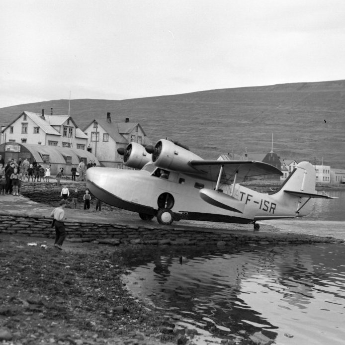 64. Gruman Goose flugbátur Flugfélags Íslands ekur upp rampinn að flugplaninu við Strandgötu 35 um 1950. Pollurinn á Akureyri var notaður til flugtaka og lendinga af öllum gerðum sjóflugvéla.  Áhorfendur eru fullnærri skrúfublöðum flugvélarinnar. Ljósmynd Eðvarð Sigurgeirsson.