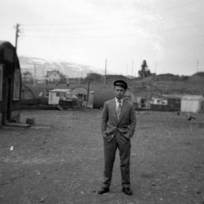 73. Prúðbúinn maður á Gleráreyrum, um 1950. Jakob Thorarensen. Braggi tv. var “Öl og gos” gosdrykkjaverksmiðjan, austan við verksmiðjur SÍS. Grjótmulningsvél fyrir miðju, þá Baldurshagi, og Brekkugata 32, th. eru kofar sem voru notaðir sem hesthús. Ljósmynd Ari Leó Björnsson.