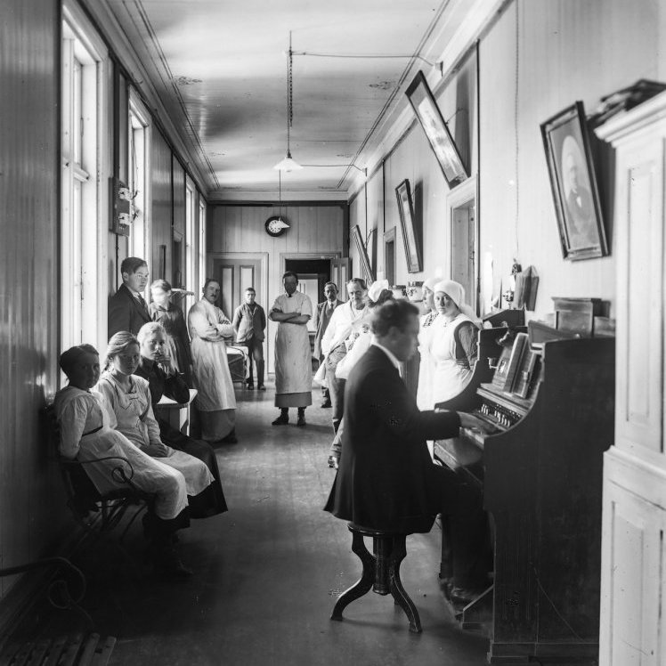 Áskell Snorrason, tónskáld og söngstjóri, leikur á orgel spítalans. Læknarnir Steingrímur Matthíasson og Jónas Rafnar sjást fjær ásamt sjúklingum og starfsfólki.