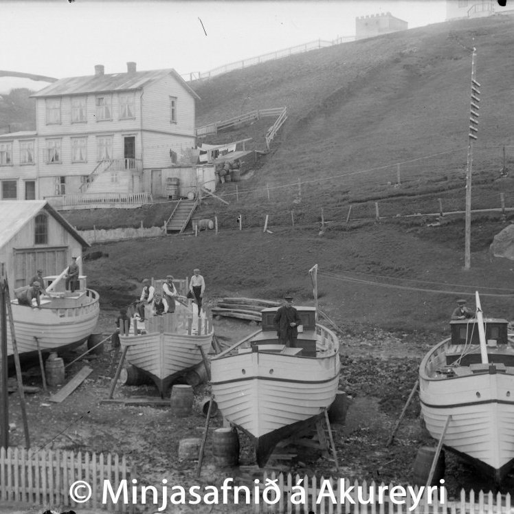 Bátasmíði á lóð Höepfners. Sláturhús Höepfners til vinstri, hús Guðmundar skósmiðs Vigfússonar ofar. Hvítklædd stúlka gengur upp Spítalaveginn framhjá stórum steini, sem börn trúðu að væri bústaður huldufólks.