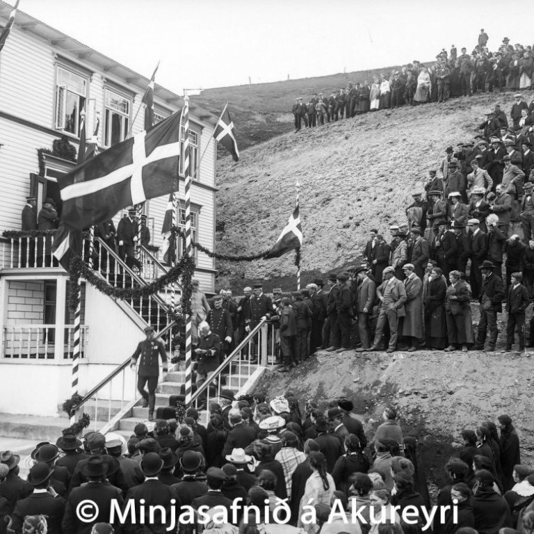 Friðrik VIII kemur frá veislu í Góðtemplarahúsinu. Prúðbúnir bæjarbúar fylgjast með.