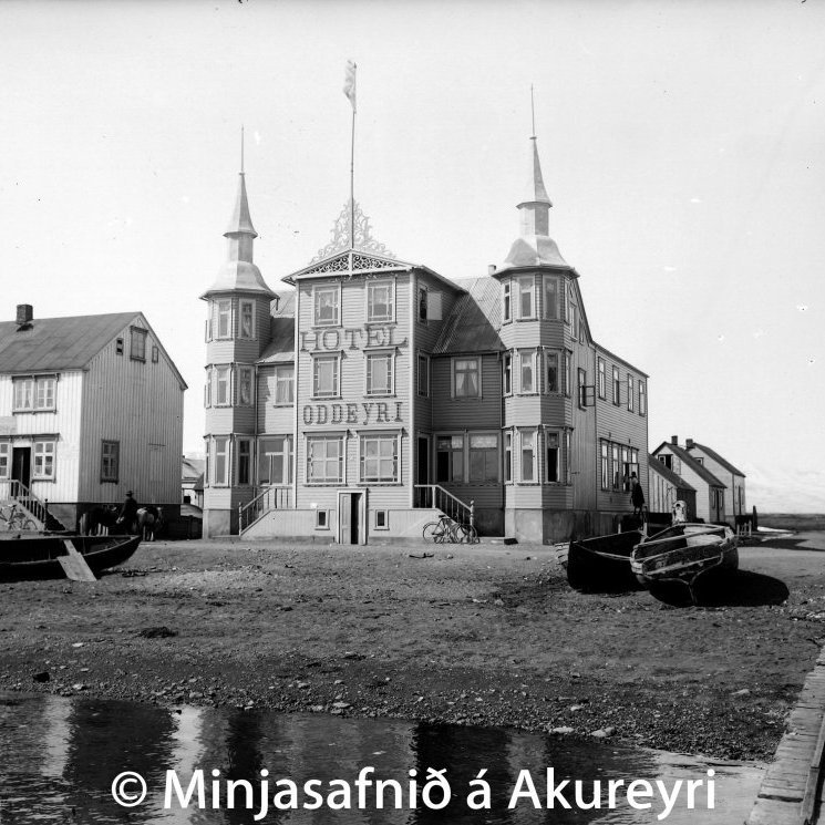Hótel Oddeyri, Strandgötu 33 og til vinstri verslun Sigurðar Fanndals, Strandgötu 31. Hótel Oddeyri var byggt árið 1884 og átti það Ólafur Jónsson veitingamaður, faðir Ragnars Ólafssonar kaupmanns. Eftir lát hans árið 1898 tók ekkja hans, Anna Tómasdóttir, við hótelinu og rak það af miklum dugnaði og atorku. Fékk hún leyfi til að stækka hótelið 1905 með viðbyggingu til norðurs meðfram Grundargötu og útbyggingu á framhlið milli turna. Þessi mynd er tekin eftir stækkunina, glæsilegt hús eins og sjá má. En dýrðin stóð ekki lengi. Hótel Oddeyri brann árið 1908 ásamt verslunarhúsi Sigurðar Fanndals.