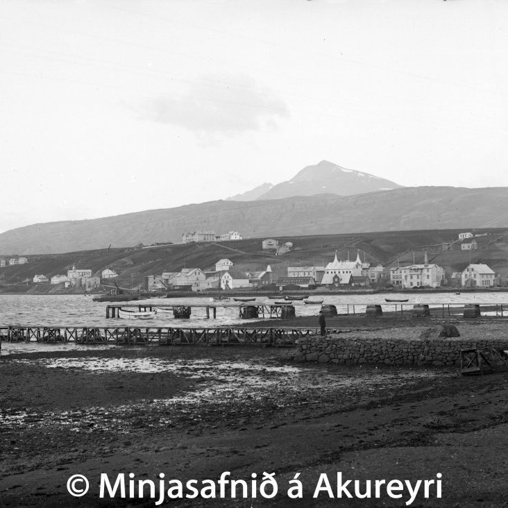 Akureyri 1915. Myndin er tekið úr Strandgötu og eru bryggjur Havsteens og Snorra Jónssonar hið næsta. Fögur fjallasýn til suðvesturs og ber Súlur við himin. Í brekkunni norðan Samkomuhússins er húsið Sjónarhæð, Hafnarstræti 63, byggt 1901. Það var íbúðarhús og samkomusalur Arthurs Gook trúboða. Í húsinu var útvarpsstöð á árunum 1926-1929, ein hin fyrst hér á landi. Gook gerði einnig tilraunir með að ná sjónvarpsútsendingum með góðum árangri. Uppi á Brekkunni sést hið glæsilega hús Gagnfræðaskólans, nú Menntaskólinn á Akureyri, en til  vinstri við það er Eyrarlandsbærinn og „Stofan“. Húsið með hvíta stafninum er Eyrarlandsvegur 26, hús Sigurðar E. Hlíðar dýralæknis og ritstjóra, nú hús kaþólska safnarðarins. Neðst við Eyrarlandsveginn er hús nr. 8, kallað Æsustaðir, byggt árið 1906, og hús nr. 4, kallað Stóruvellir, byggt árið 1902. Neðar til vinstri er hús séra Matthúasar, Sigurhæðir, byggt árið 1903. Norðan við Grófargilið eru húsið Garður (ofar) og tvö hús á svokölluðu Skessunefi, nú við Gilsbakkaveg.