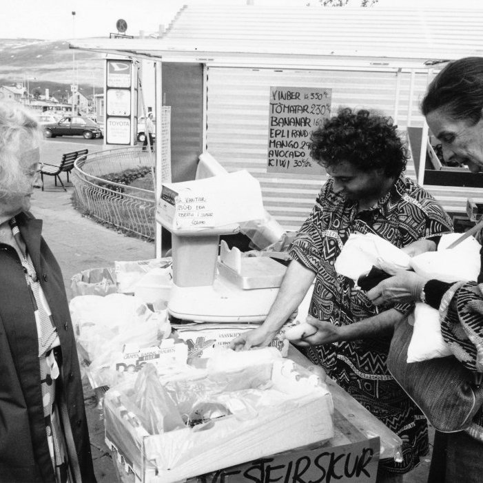 19.	Hver man ekki eftir glaðlynda ítalska ávaxtakaupmanninum Cosimo og verslun hans á Ráðhústorgi?  Þar seldi hann gestum og gangandi úrval að grænmeti og ávöxtum frá 1982-1984 og aftur árið 1989. Cosimo kynnti fyrir Akureyringum ýmsa framandi ávexti. Eitt sinn kom bóndi til Cosimo og spekuleraði lengi í kiwi ávöxtunum og sagði svo “Heyrðu, frá hvaða landi koma þessar loðnu kartöflur eiginlega?”. Hér er Signý Stefánsdóttir að kanna úrvalið hjá Cosmio 7.júlí 1989. Ljósmyndari Kristján Logason.